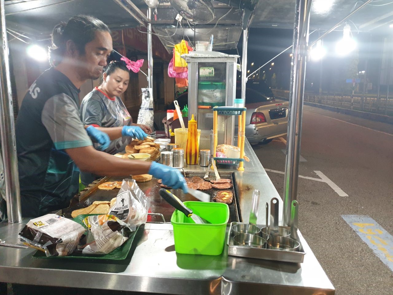 Gambar menunjukkan penjual burger sedang sibuk memasak burger untuk pelanggan-pelanggan